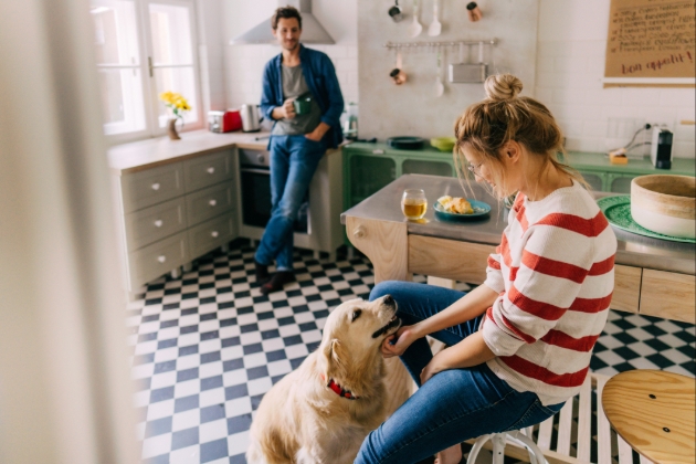 Lady sits and strokes her dog in the kitchen whilst partner drinks coffee