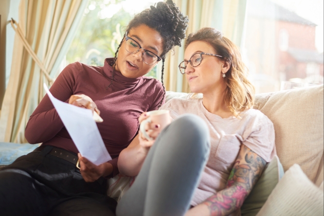 Two women look at paperwork whilst sitting on sofa