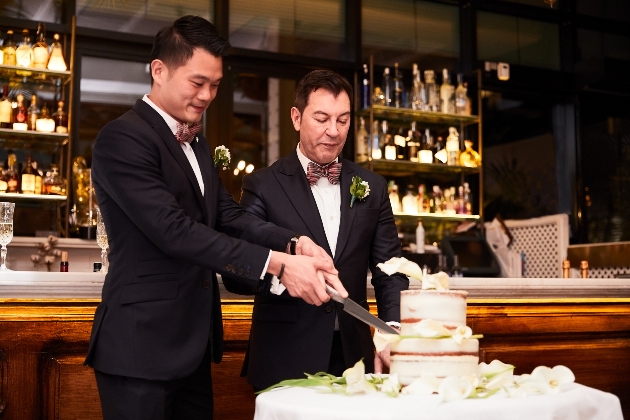 two men cutting wedding cake in wedding suits