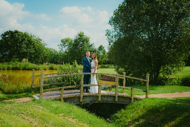 Bride and groom pose on arched bridge over river