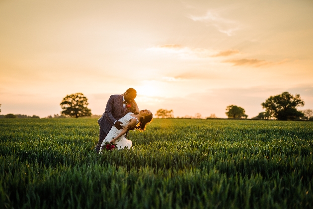 Bride and groom pose in a field at sunset