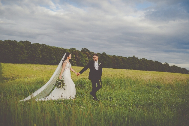 Groom leads Bride through green fields