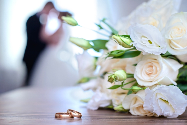 a white rose bouquet laying on a table with two wedding rings in front of it 