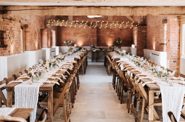 Two long wooden tables decorated with flowers and cloths inside a barn