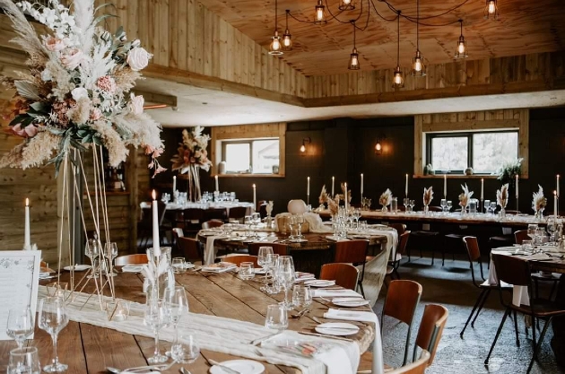 The interior of a barn decorated with round tables, chairs and flowers