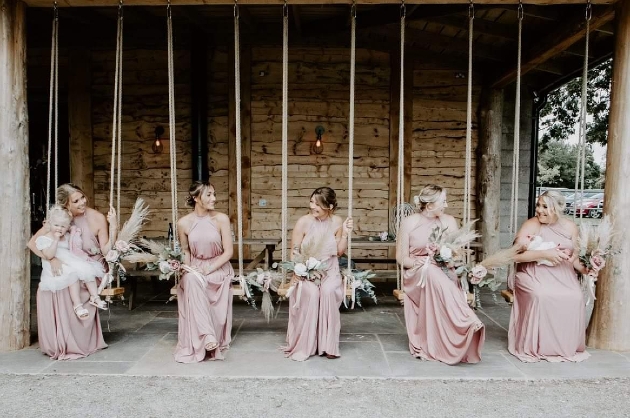 Five bridesmaids sitting on swings smiling at each other