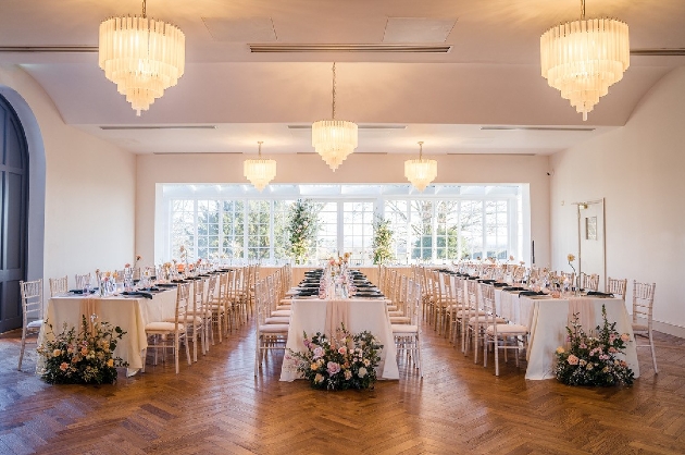 A white room with a wooden floor decorated with three long tables and flowers