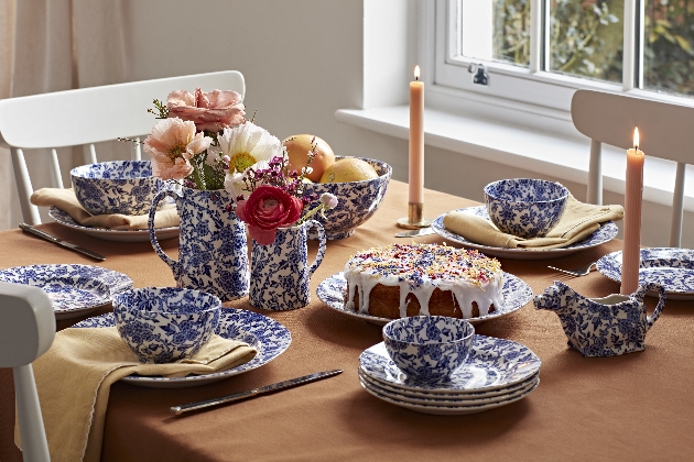 White and blue crockery set up on a table with cake, candles and flowers