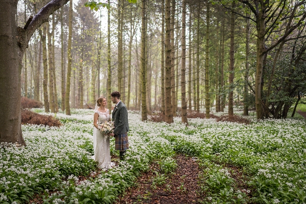 A bride and groom standing close to each other in a forest